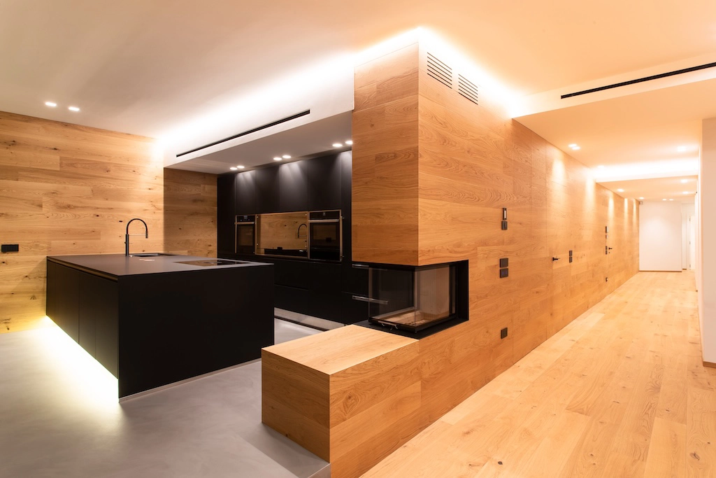 Casa BN — side view of black kitchen with integrated fireplace and oak wood-clad corridor, interior design Vicenza