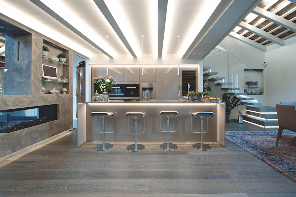 Casa SM — penthouse with illuminated island kitchen, steel stools, stone fireplace and cantilevered staircase, interior design Vicenza