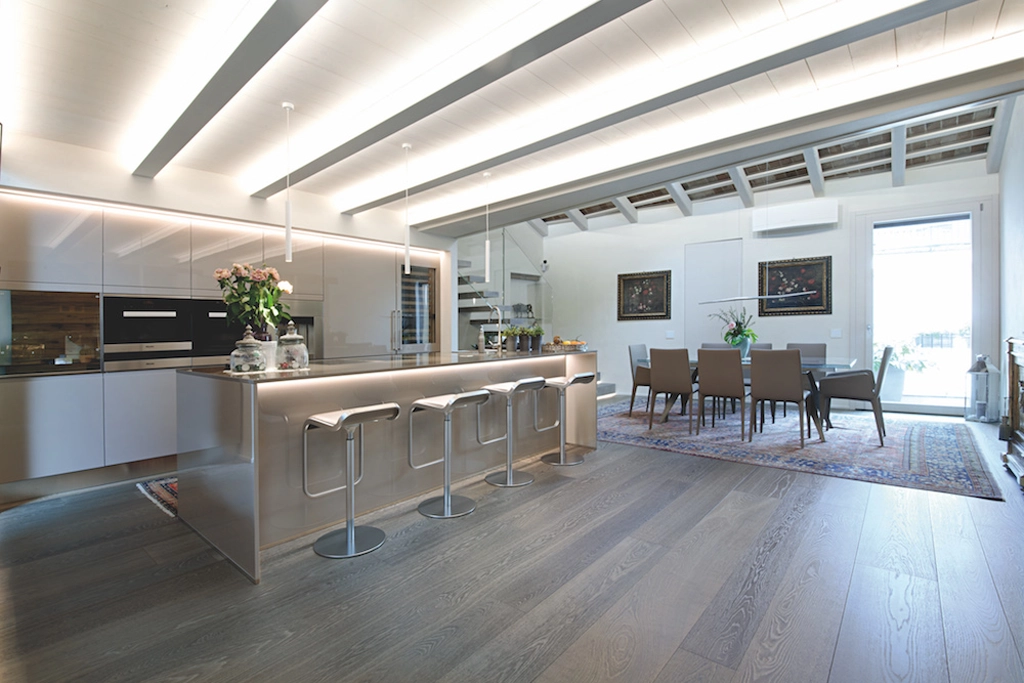 Casa SM — penthouse with steel island kitchen, dining room with table and brown chairs and grey oak parquet, interior design Vicenza