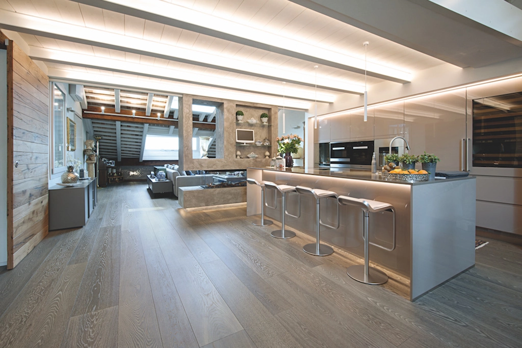 Casa SM — open plan penthouse with steel island kitchen, grey oak parquet and living room in the background, interior design Vicenza