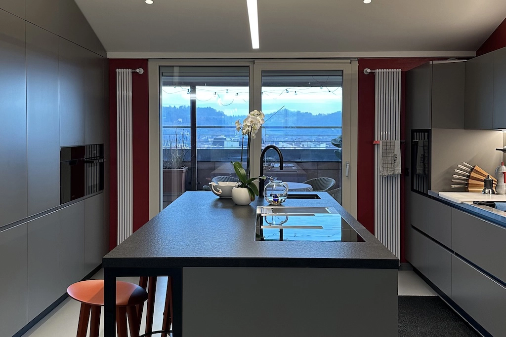 Casa BB — grey island kitchen with dark stone worktop, red stool and terrace view, interior design Vicenza